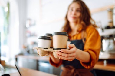 Genç bayan barista elinde tek kullanımlık bardakla sıcak bir içecek tutuyor. Paket teslimat konsepti. Paket yemek kavramı, iş