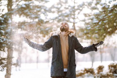 Karlı bir ormanda genç şık bir adam. Yakışıklı adam güneşli kış havasının tadını çıkarıyor. İnsan kavramı, tatil..