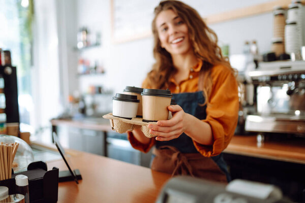 Young female barista holding disposable glasses with hot drink to go. Takeaway delivery concept. Takeaway food concept, business