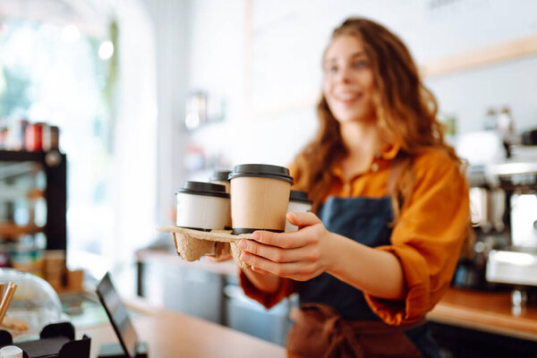Young female barista holding disposable glasses with hot drink to go. Takeaway delivery concept. Takeaway food concept, business