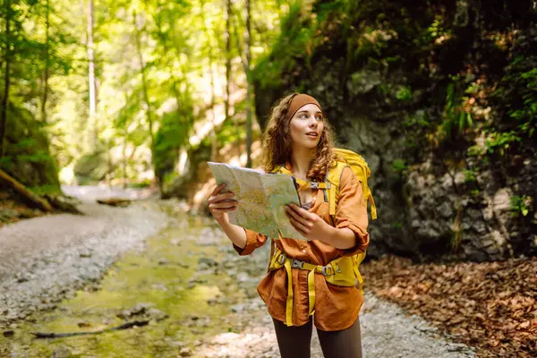 A young woman on a mountain path with a map in her hands, exploring hiking trails. A traveler uses a map to navigate the mountain trails. Adventure concept.