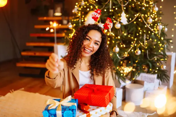 stock image Happy woman holding sparkler and Christmas gifts at home near New Year tree. Holiday concept. The winter vacation.