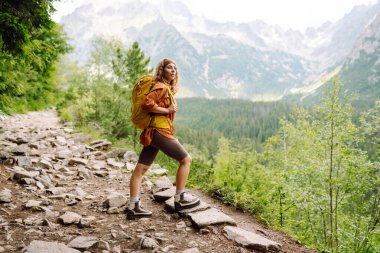 Uçurumun tepesinde sarı sırt çantalı genç bir gezgin kadın dağ manzarasının keyfini çıkarıyor. Spor anlayışı, gezgin. Etkin yaşam biçimi.