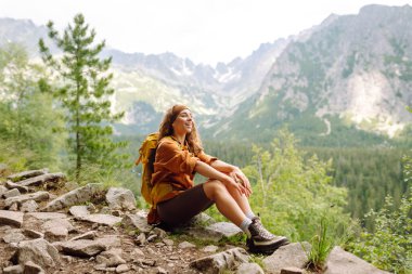 Uçurumun tepesinde sarı sırt çantalı genç bir gezgin kadın dağ manzarasının keyfini çıkarıyor. Spor anlayışı, gezgin. Etkin yaşam biçimi.