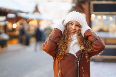 Dekorasyon ve ışıklarla süslenmiş genç bir kadın Noel pazarında yürüyor. Şenlikli bir markette poz veren mutlu bir kadın. Tatil konsepti, rahatlama..