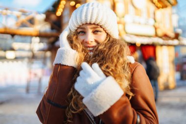 Dekorasyon ve ışıklarla süslenmiş genç bir kadın Noel pazarında yürüyor. Şenlikli bir markette poz veren mutlu bir kadın. Tatil konsepti, rahatlama..