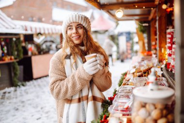 Mutlu kadın bardaktan sıcak bir içecek içer ve güneşli bir kış gününde Noel pazarında yürür. Kış tatilini geçirmek. Tatil kavramı.