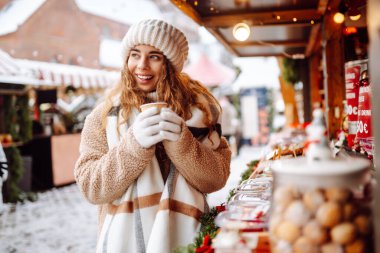 Mutlu kadın bardaktan sıcak bir içecek içer ve güneşli bir kış gününde Noel pazarında yürür. Kış tatilini geçirmek. Tatil kavramı.