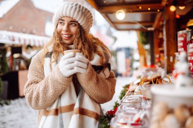 Mutlu kadın bardaktan sıcak bir içecek içer ve güneşli bir kış gününde Noel pazarında yürür. Kış tatilini geçirmek. Tatil kavramı.