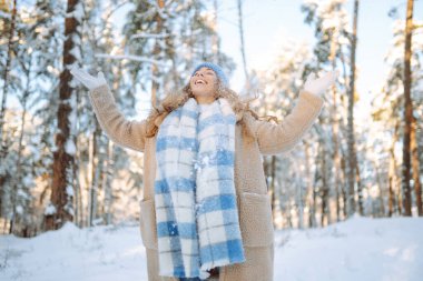 Genç bir kadın kar atıyor. Güneşli bir kış gününde karla oynayan mutlu bir kadının portresi. Kış ormanında bir yürüyüş. Eğlence kavramı, rahatlama..