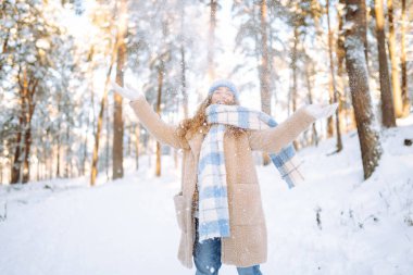 Genç bir kadın kar atıyor. Güneşli bir kış gününde karla oynayan mutlu bir kadının portresi. Kış ormanında bir yürüyüş. Eğlence kavramı, rahatlama..