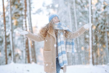Genç bir kadın kar atıyor. Güneşli bir kış gününde karla oynayan mutlu bir kadının portresi. Kış ormanında bir yürüyüş. Eğlence kavramı, rahatlama..