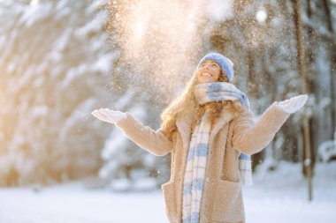 Genç bir kadın kar atıyor. Güneşli bir kış gününde karla oynayan mutlu bir kadının portresi. Kış ormanında bir yürüyüş. Eğlence kavramı, rahatlama..