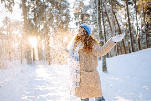 A young woman throws out snow. Portrait of a happy woman playing with snow on a sunny winter day. A walk through the winter forest. Concept of fun, relaxation.