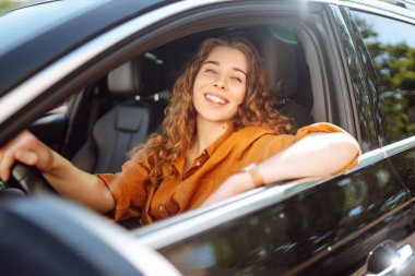 Araba süren genç ve güzel bir kadının portresi. Mutlu kadın günlük giysiler içinde arabayla seyahat ediyor. Araba yolculuğu konsepti. Yaşam biçimi.