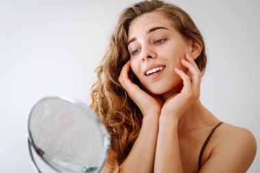 Dermatoloji. Güzel bir kadın aynaya bakıyor, elleriyle yüzüne dokunuyor, sivilceleri ve pigmentasyonu inceliyor. Kozmetik bakım. Alerjik reaksiyon. Sağlık konsepti, kozmetoloji.
