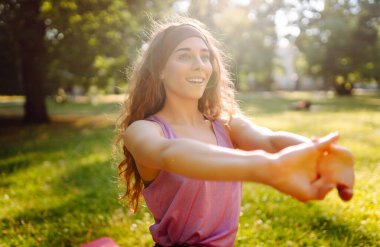Yoga yapan genç bir kadın, parkta esneme hareketleri yapıyor. Spor giyim sektöründe güzel bir kadın açık havada antrenman yapıyor. Spor, spor konsepti.