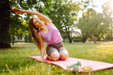 Yoga yapan genç bir kadın, parkta esneme hareketleri yapıyor. Spor giyim sektöründe güzel bir kadın açık havada antrenman yapıyor. Spor, spor konsepti.