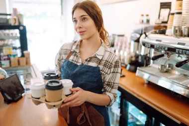 Bayan barista tek kullanımlık bardakları tutuyor. Barın arkasındaki genç barista sahibi paket sipariş veriyor. İş konsepti. Paket içecekler..