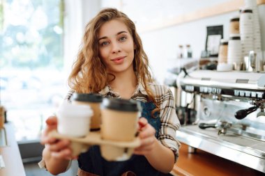 Bayan barista tek kullanımlık bardakları tutuyor. Barın arkasındaki genç barista sahibi paket sipariş veriyor. İş konsepti. Paket içecekler..