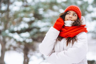 Karlı bir ormanda kırmızı şapkalı güzel bir kadının portresi. Genç bir kadın kış günü karla eğleniyor. Tatil konsepti, doğa.