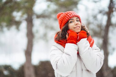 Karlı bir ormanda kırmızı şapkalı güzel bir kadının portresi. Genç bir kadın kış günü karla eğleniyor. Tatil konsepti, doğa.