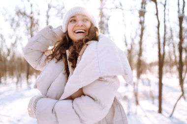 Kış yürüyüşü. Kışlık giysiler içinde gülümseyen bir kadın güneşli bir günde karlı bir ormanda yürür. Yürüme, seyahat kavramı.