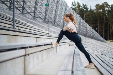 Spor giyim sektöründe çekici genç bir kadın açık havada esniyor. Bir atlet spor sahasında egzersiz yapar. Sağlık konsepti. Etkin yaşam biçimi.