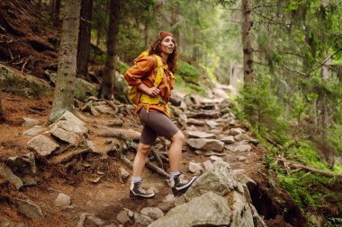 Gülümseyen bir kadın gezgin dağlarda yürüyüş parkurunda doğanın arka planına karşı. Sırt çantalı genç bir kadın dışarı çıkıyor. Yürüyüş, aktif yaşam tarzı.