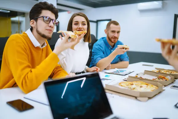 Cheerful diverse employees eating pizza together during a break in the office. Young people at a meeting in the office had a coffee break. Concept of business, negotiations.