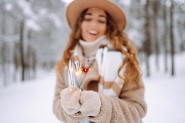 Havalı bir palto ve şapkalı şık bir kadın, karlı bir ormanda maytapları elinde tutuyor. Yeni yıl sprey şişesiyle eldivenli genç bir bayan turist. Tatil kavramı.