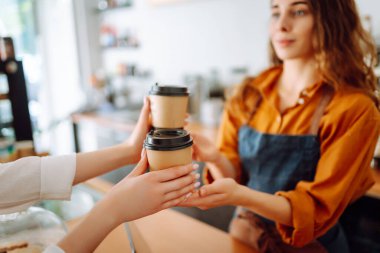 Bayan bir baristanın ellerinin yakın çekimi hazır içkileri uzatıyor. Barın arkasında bir kafe sahibi genç bir kadın kahve hazırlıyor. Sipariş verme kavramı.