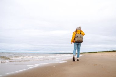 Rüzgarlı, soğuk bir sahilde çekici bir kadın. Şık giyinmiş güzel bir turist kadın deniz kenarında hayatın tadını çıkarıyor. Seyahat, doğa konsepti..