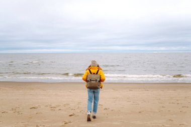 Rüzgarlı, soğuk bir sahilde çekici bir kadın. Şık giyinmiş güzel bir turist kadın deniz kenarında hayatın tadını çıkarıyor. Seyahat, doğa konsepti..