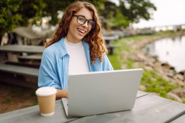 İnternette dizüstü bilgisayar kullanarak çalışan ve göle bakan doğal manzaranın tadını çıkaran güzel bir kadın ressamın portresi. Serbest konsept, doğa.