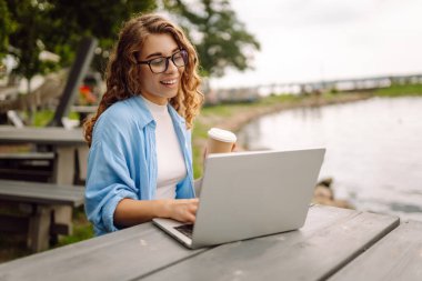 İnternette dizüstü bilgisayar kullanarak çalışan ve göle bakan doğal manzaranın tadını çıkaran güzel bir kadın ressamın portresi. Serbest konsept, doğa.