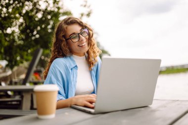 İnternette dizüstü bilgisayar kullanarak çalışan ve göle bakan doğal manzaranın tadını çıkaran güzel bir kadın ressamın portresi. Serbest konsept, doğa.