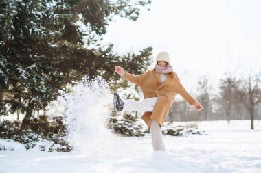 Kış gülüşlü, kıvırcık saçlı ve güneşli bir günde karlı bir ormanda karla eğlenen bir kadın. Rahatlama kavramı, eğlence.