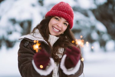 Karlı bir parkta eğlenen mutlu genç bir kadının portresi. Kırmızı şapkalı ve eşarplı mutlu kadın dışarıda yürüyor..