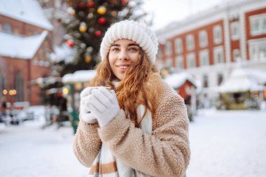 Genç bir kadın Noel pazarında sıcak bir içecek içiyor. Akşamları festival ışıklarıyla süsleniyor. Tatil konsepti, hafta sonları, rahatlama..