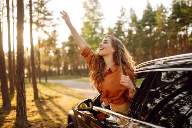 Genç bir kadın araba penceresinden güneşli havanın tadını çıkarıyor. Mutlu turistler arabayla seyahat eder. Macera konsepti. Etkin yaşam biçimi.