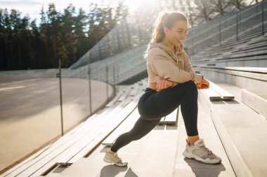 Spor giyimli genç bir kadın dışarıda antrenman yapıyor. Akıllı saati olan fitness kadını spora gider, esneme egzersizleri yapar. Spor konsepti, sağlıklı vücut.