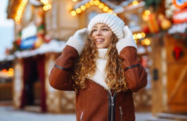 Eldivenli mutlu kadın Noel pazarının karlı caddesinde yürüyor. Genç bayan turist açık havada karlı havanın tadını çıkarıyor. Tatil konsepti, yürü.