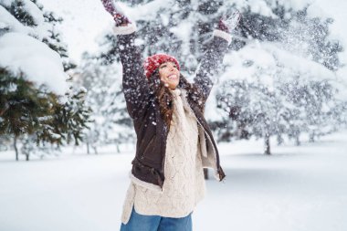 Kırmızı şapkalı ve eşarplı mutlu kadın kış parkında karla oynuyor. Rahatlama kavramı, eğlence.