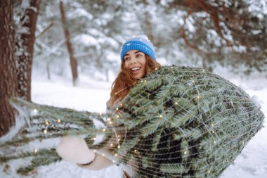 Mutlu kadın, karlı bir ormanda bir Noel ağacı taşıyor. Genç bir kadın dışarıda tatil yapmaktan hoşlanıyor. Doğa kavramı, mutluluk..