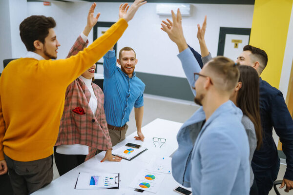 A group of people in an office meeting collectively resolve an issue by raising their hands. Colleagues in the office sign an agreement, hands forward. Concept of business, negotiations.