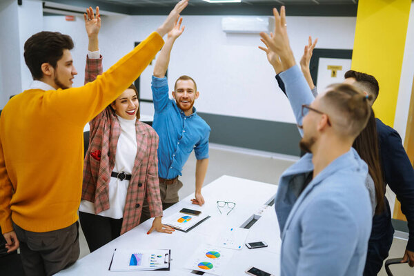 A group of people in an office meeting collectively resolve an issue by raising their hands. Colleagues in the office sign an agreement, hands forward. Concept of business, negotiations.
