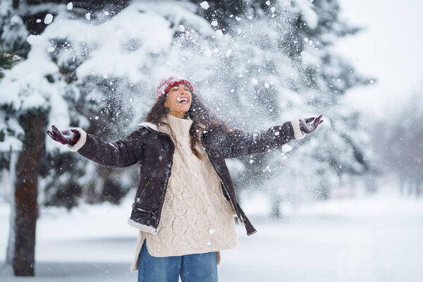 Happy woman in a red hat and scarf plays with snow in a winter park. Concept of relaxation, fun.