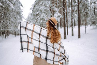 Kış ormanında güzel bir kadın dondurucu havanın tadını çıkarıyor. Şapka, ekose atkı ve palto giyen genç bir kadın. Kış tatilin kutlu olsun. Noel.