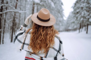 Kış ormanında güzel bir kadın dondurucu havanın tadını çıkarıyor. Şapka, ekose atkı ve palto giyen genç bir kadın. Kış tatilin kutlu olsun. Noel.